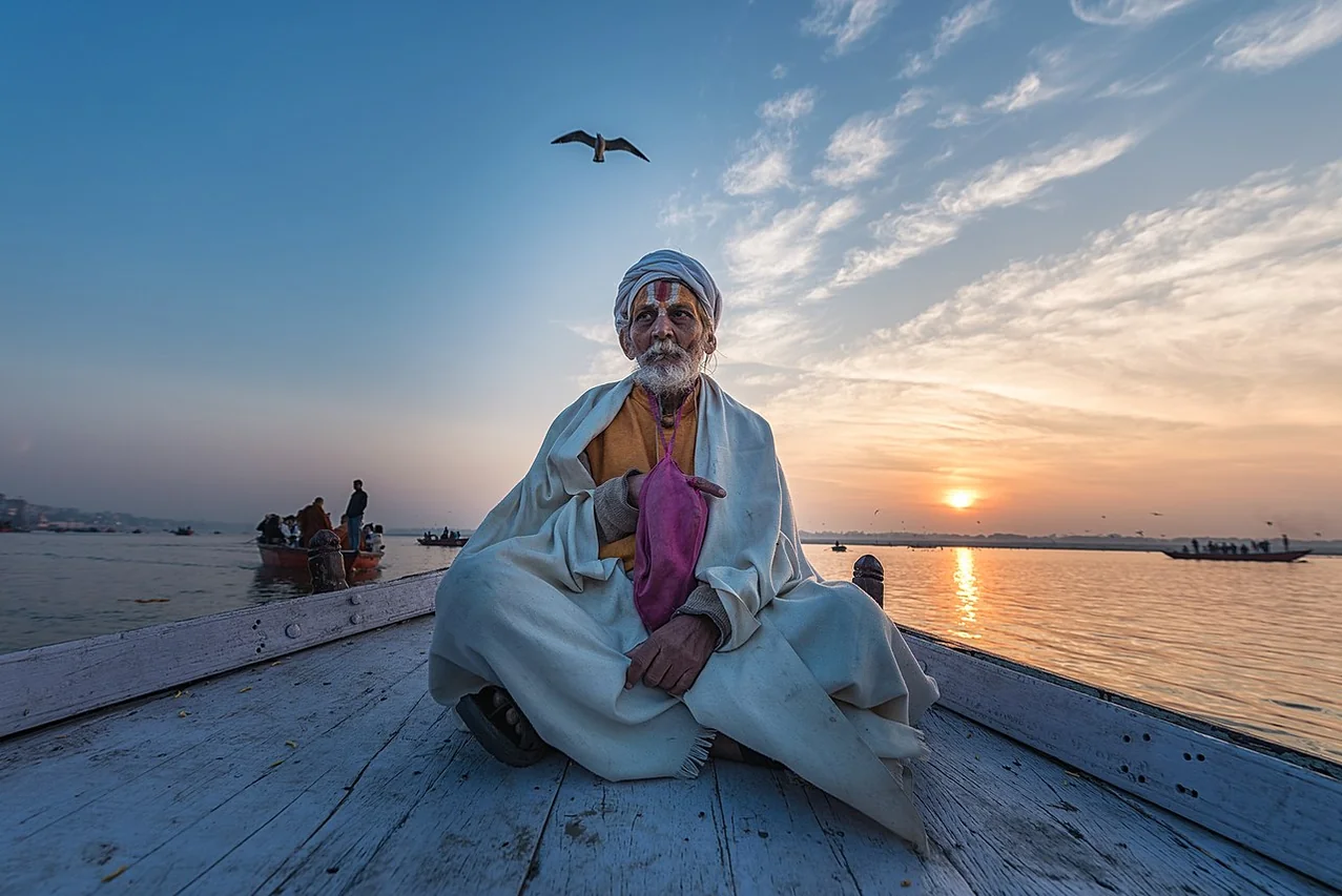 Ancient Varanasi city architecture and Ganges river ghat at sunset with view of an Indian sadhu sitting a boat on the river Ganges.